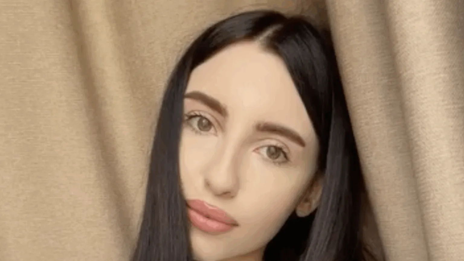 Жінка з темним волоссям перед бежевою завісою