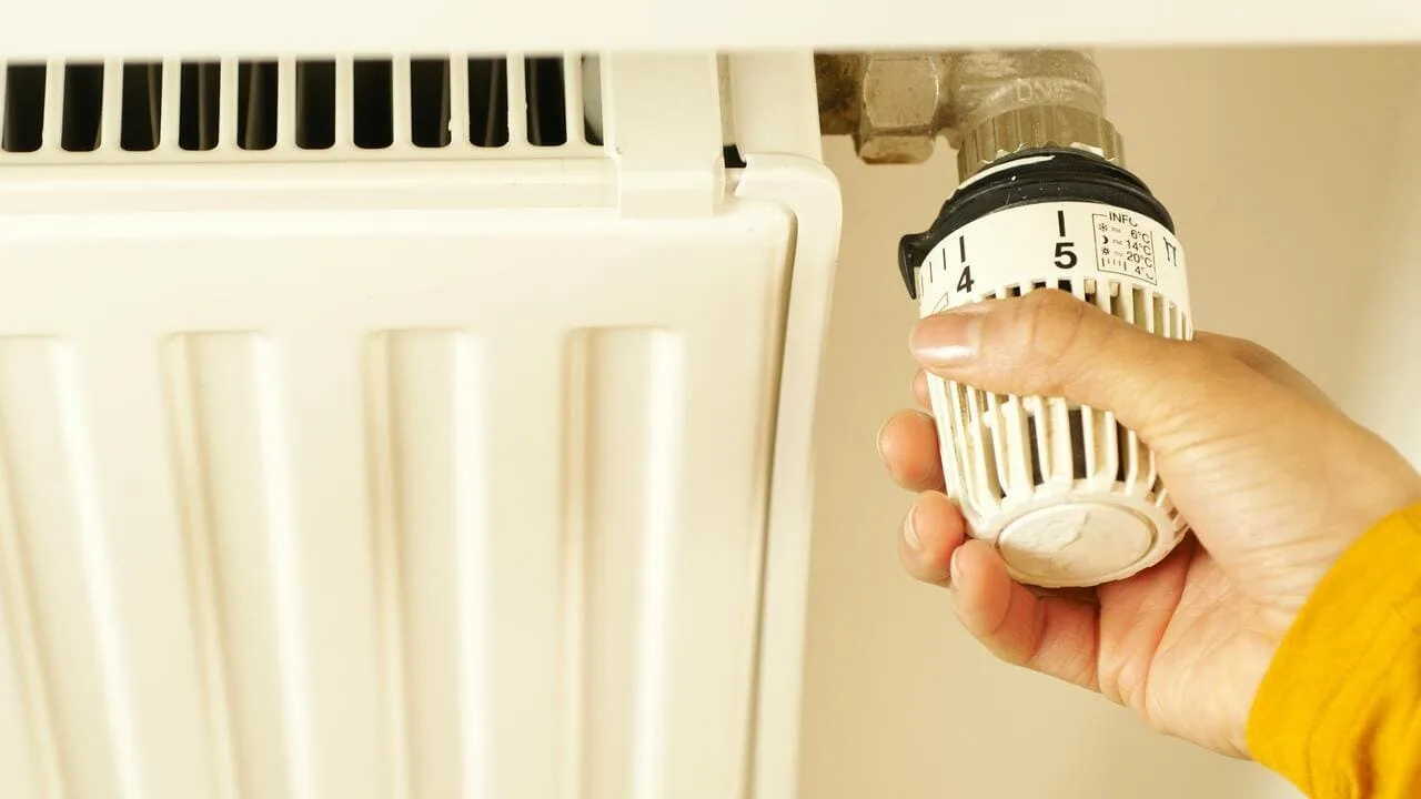 Рука регулює температуру на радіаторі опалення