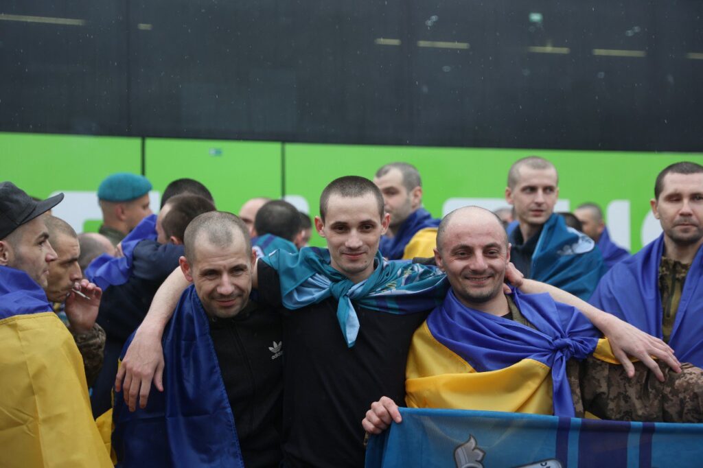 Група чоловіків з українськими прапорами, обіймаються.
