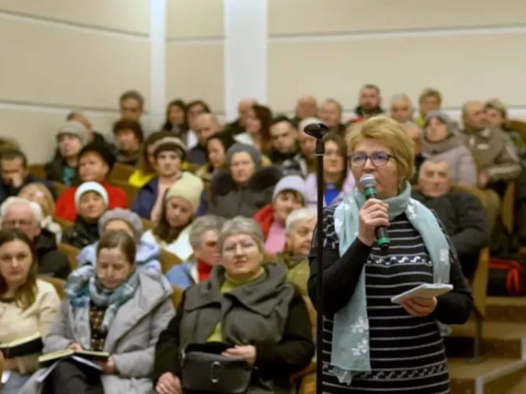 Жінка говорить у мікрофон перед аудиторією людей