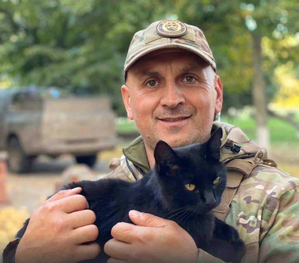 Військовий тримає чорного кота на вулиці