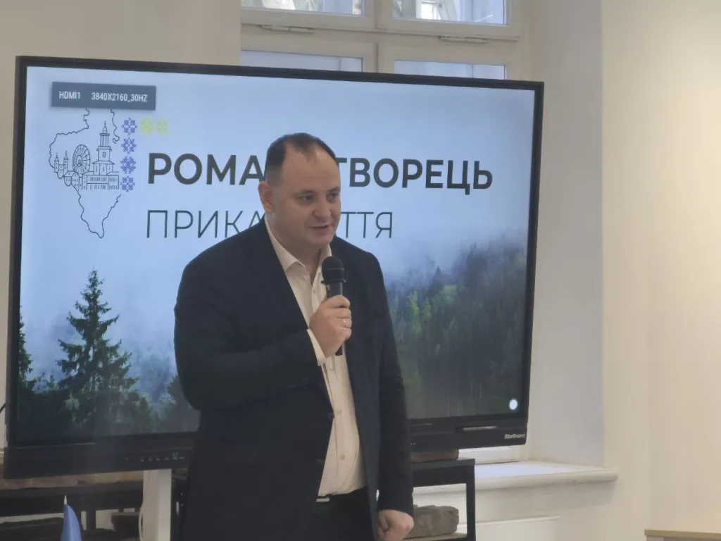 Чоловік виступає з мікрофоном перед екраном
