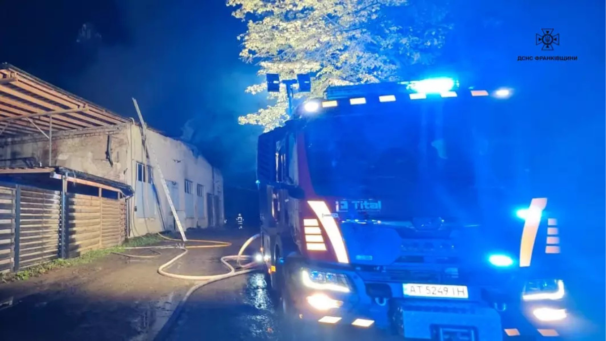 Пожежна машина біля палаючої будівлі вночі.