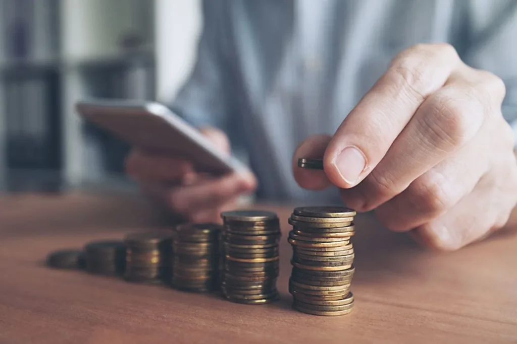 Людина рахує монети та користується смартфоном
