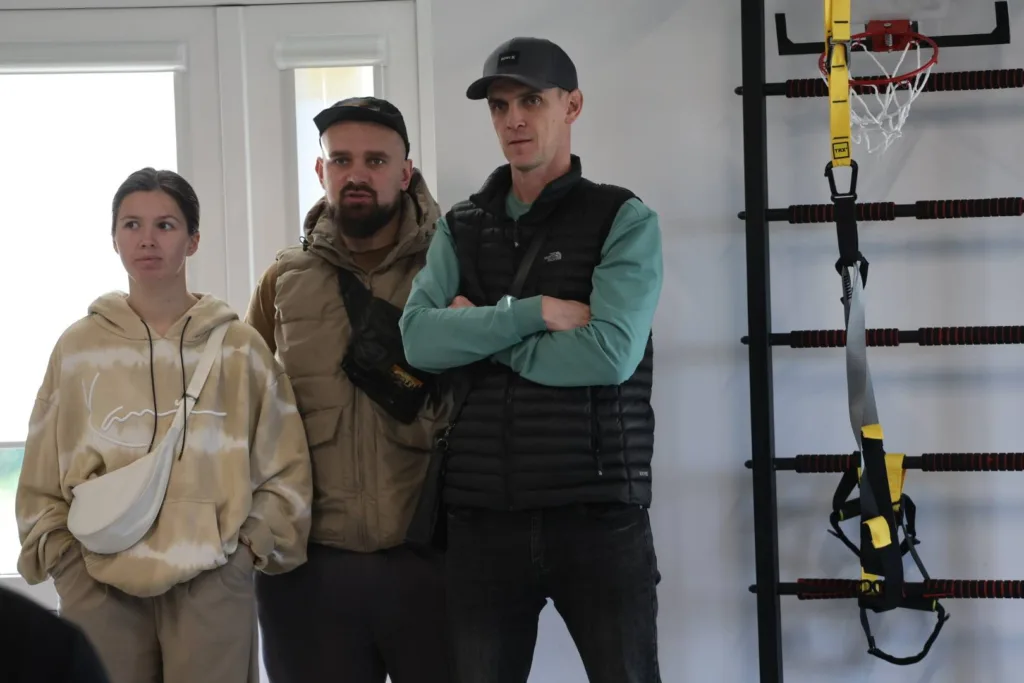 Троє людей стоять біля спортивного обладнання в приміщенні