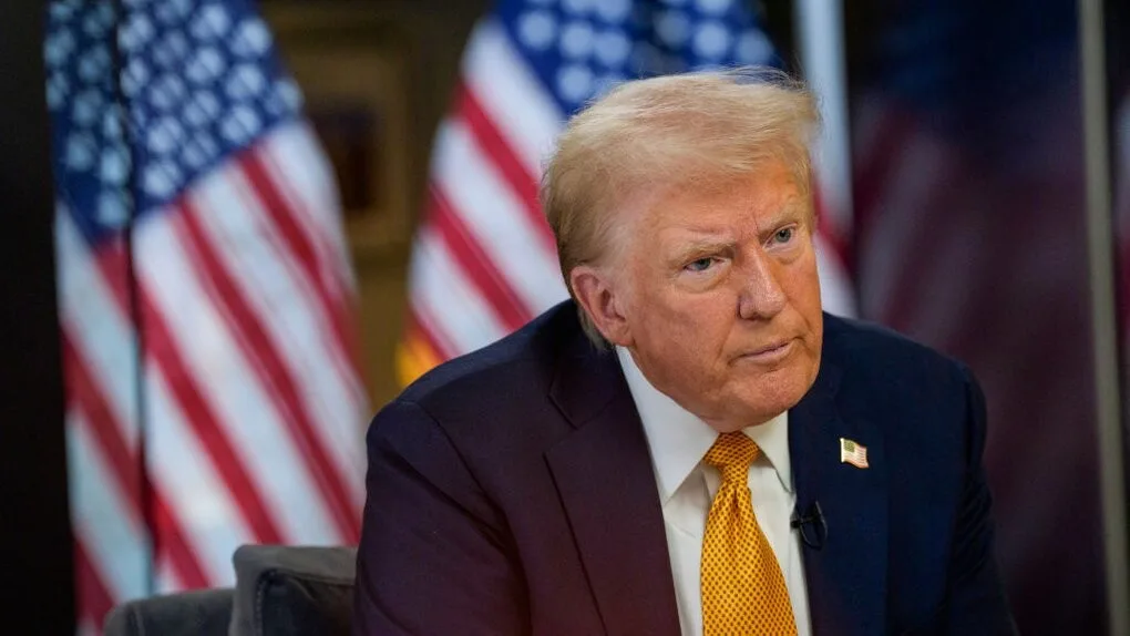 Чоловік у костюмі перед прапорами США