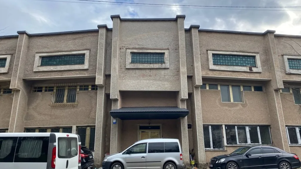 Фасад сірої будівлі з припаркованими автомобілями