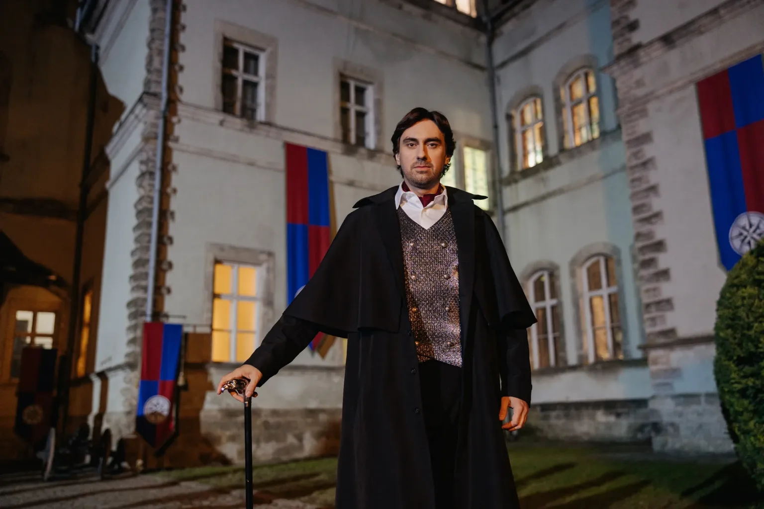 Чоловік у плащі стоїть перед старовинним будинком