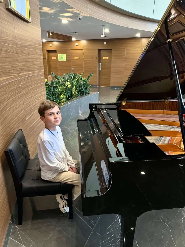 Хлопчик сидить за роялем у сучасній залі