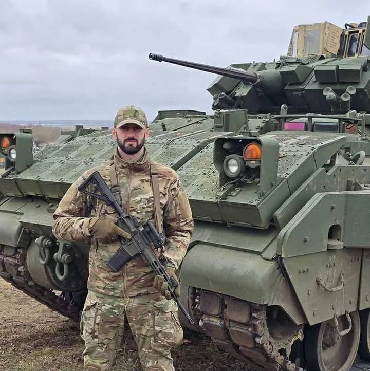 Військовий стоїть перед бронетехнікою на полі