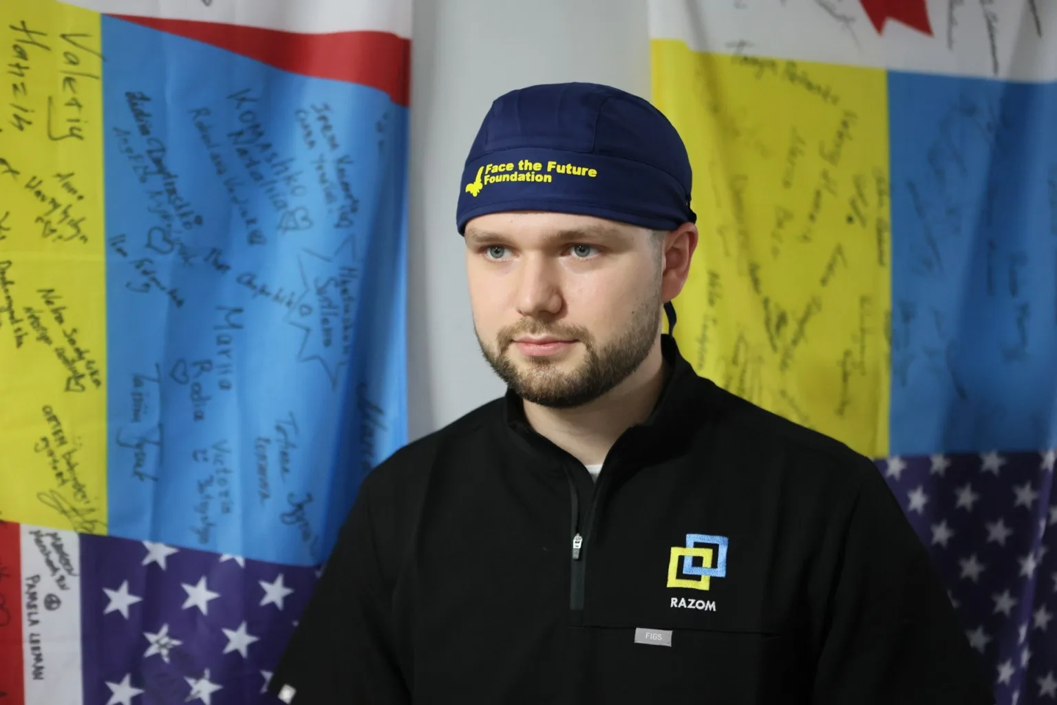 Волонтер організації Razom перед підписаними прапорами