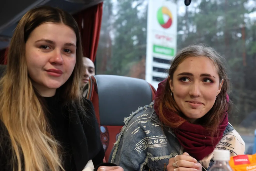 Дві дівчини сидять у автобусі, емоційно посміхаються.