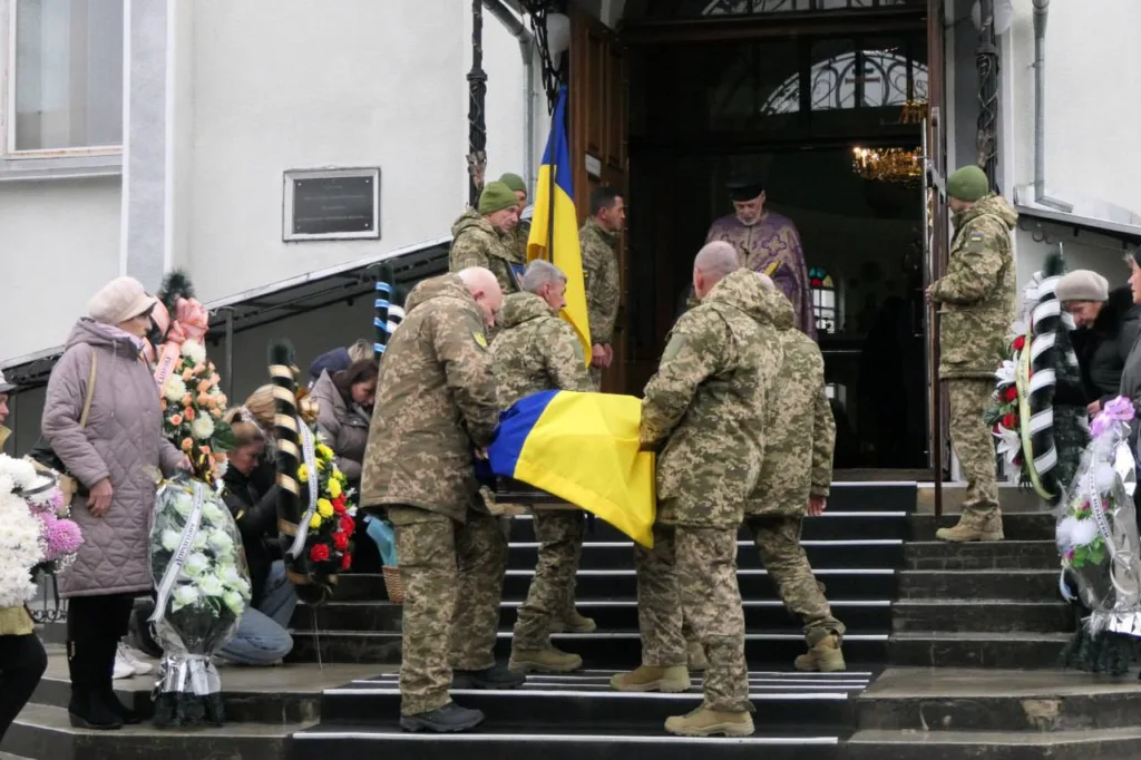 Військові несуть труну, накриту українським прапором