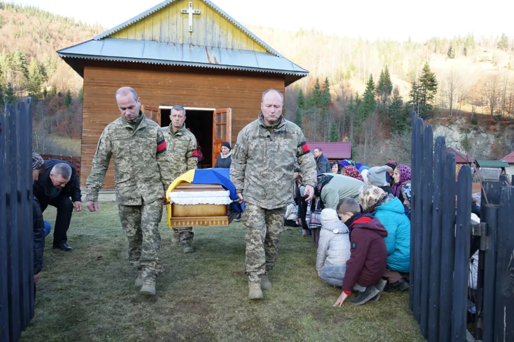 Військові несуть труну, люди схиляються у прощанні