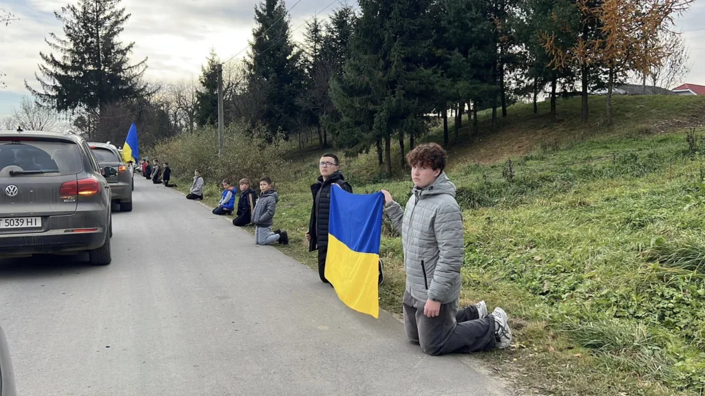 Люди на колінах з прапором України біля дороги