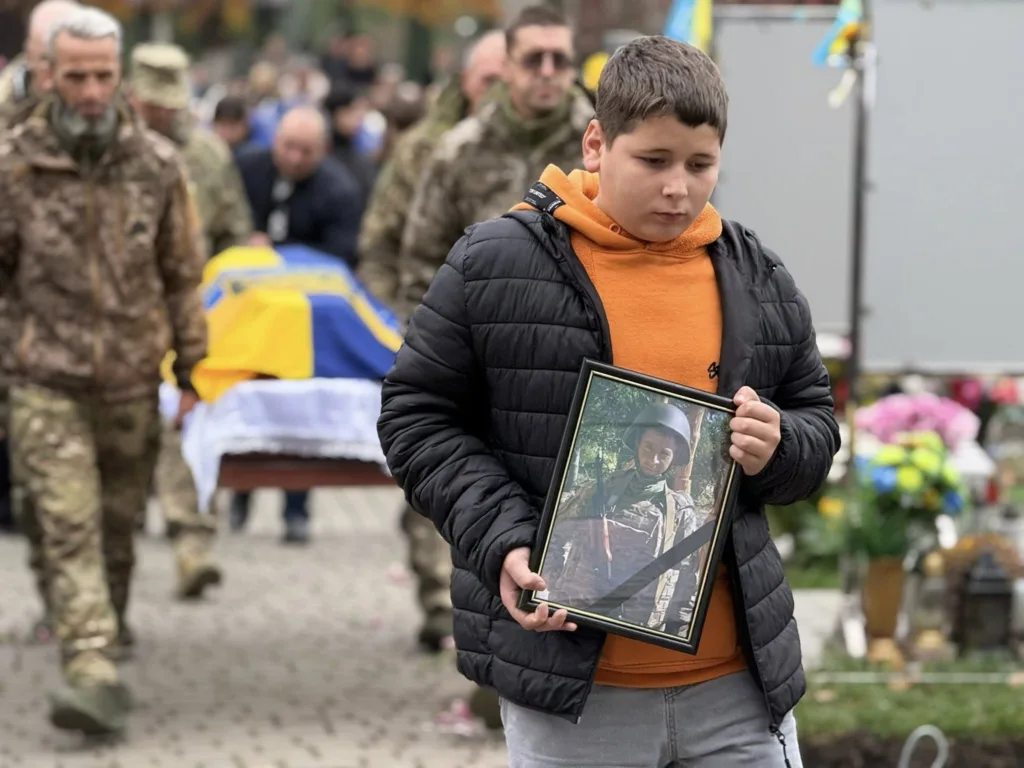 Хлопчик тримає фото військового на похороні