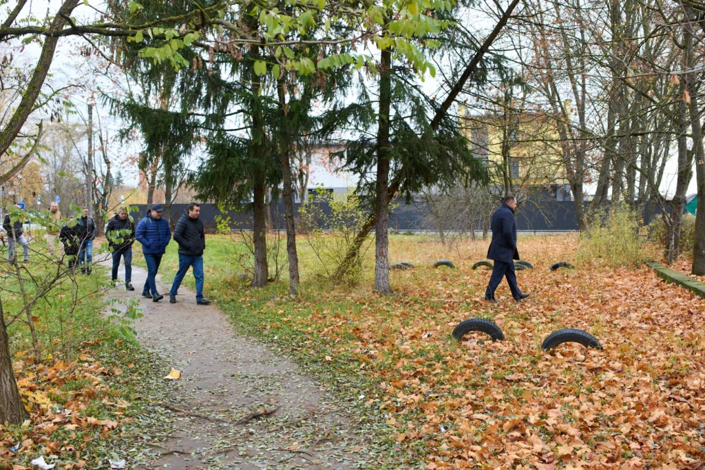 Люди гуляють парком восени серед листя.