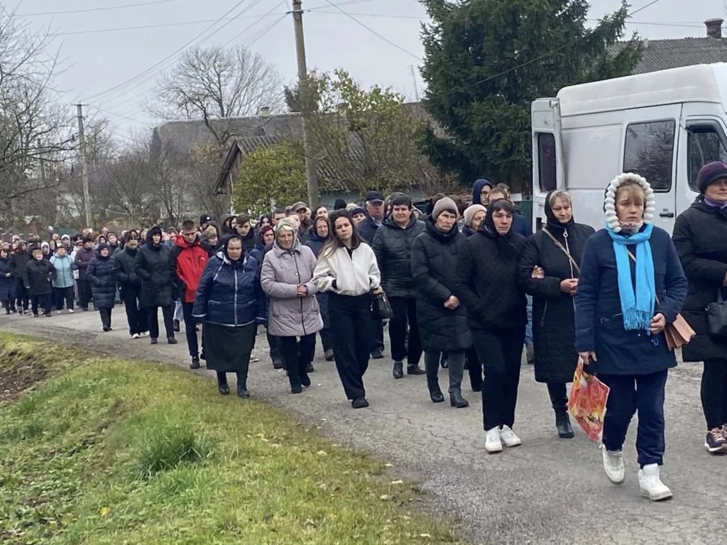 Люди йдуть дорогою під час похоронної процесії