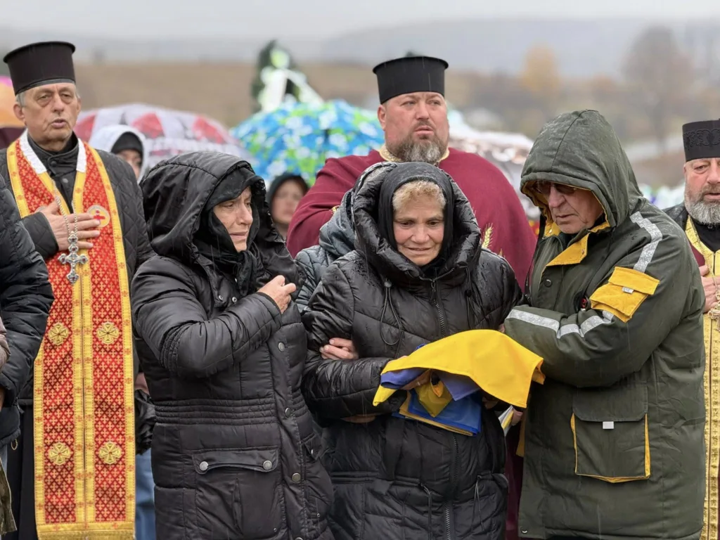 Люди на похороні з українським прапором під дощем