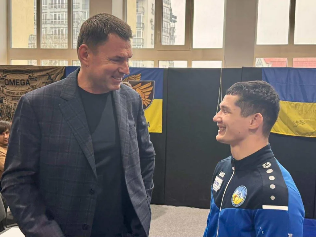 Двоє чоловіків усміхаються перед українським прапором