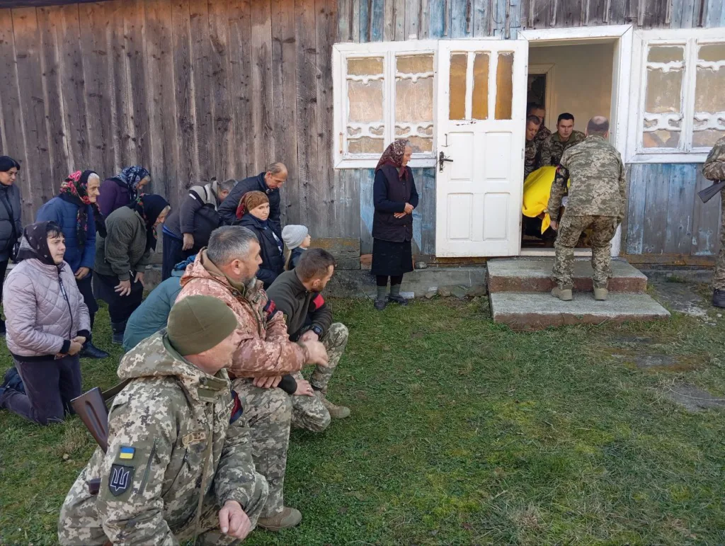 Військові й люди біля старої дерев’яної будівлі