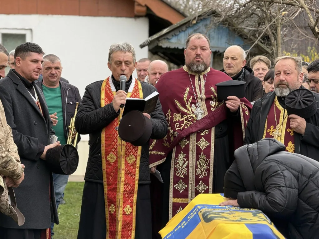 Священики проводять похоронну церемонію з прапором України.
