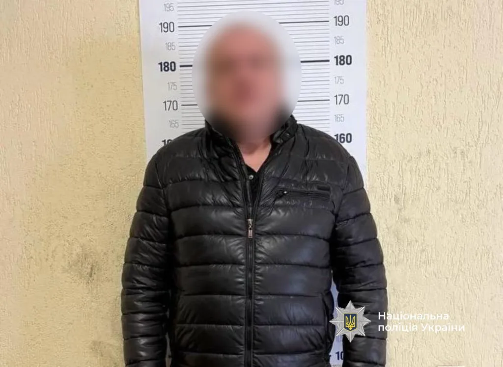 Чоловік у чорній куртці перед лінійкою зросту