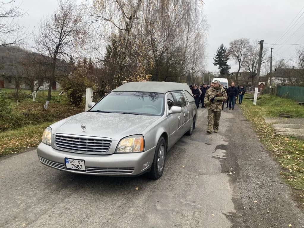 Похоронна процесія з військовим і катафалком на дорозі