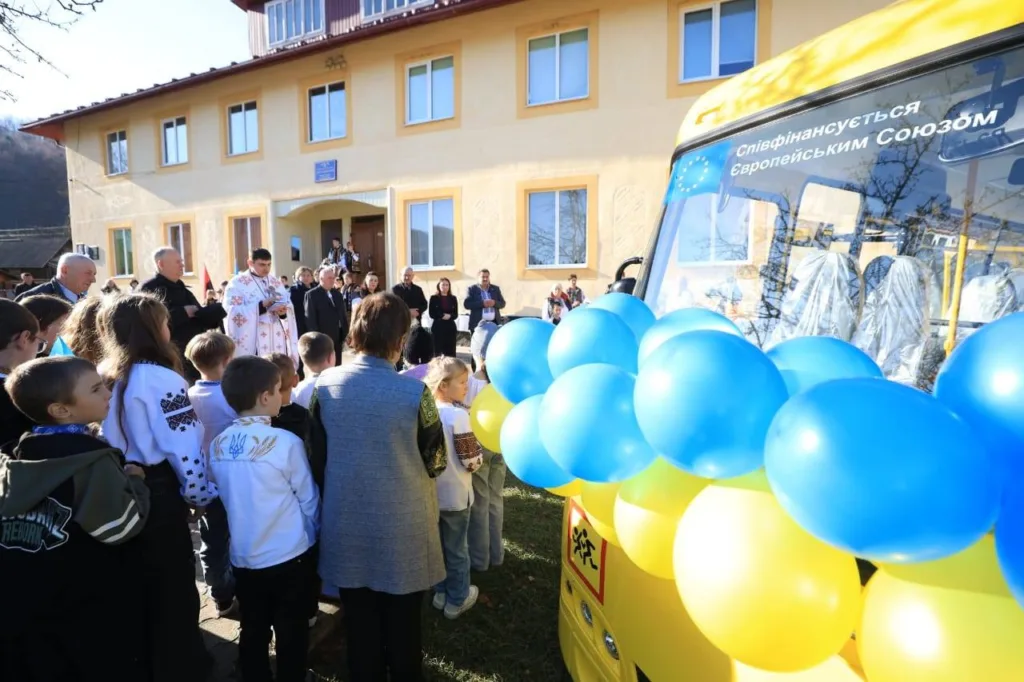 Діти біля шкільного автобуса прикрашеного синьо-жовтими кулями