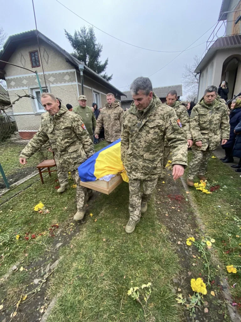 Військові несуть труну, накриту українським прапором