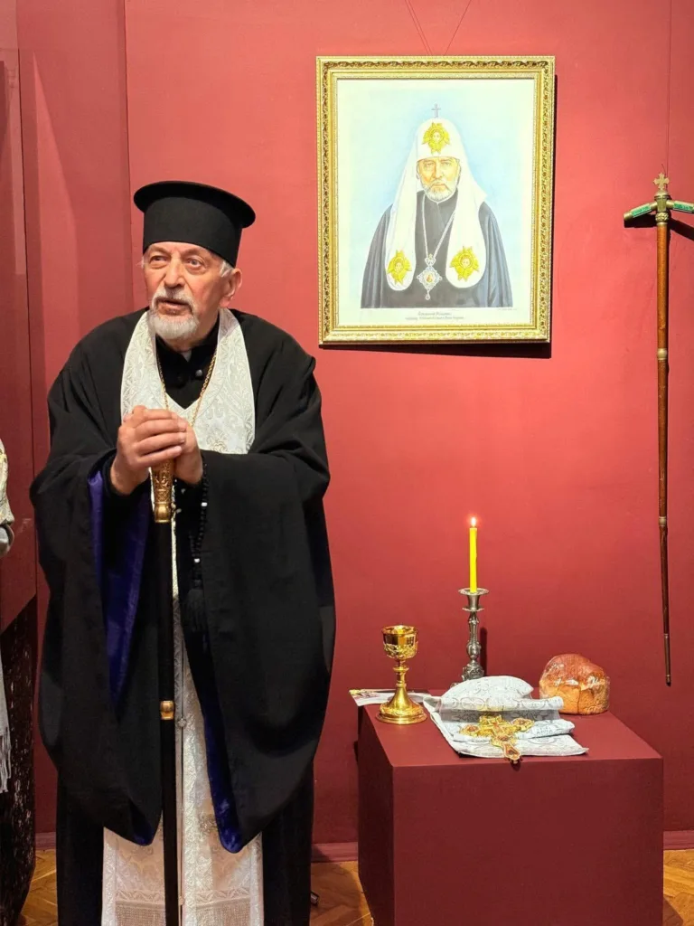 Священник у чорному облаченні біля ікони та вівтаря