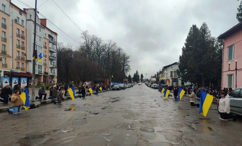 Люди на колінах з українськими прапорами на вулиці