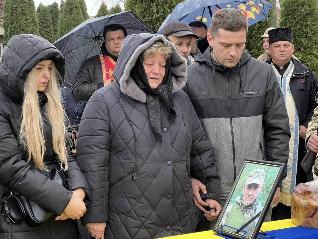 Люди сумують на похороні біля фото військового