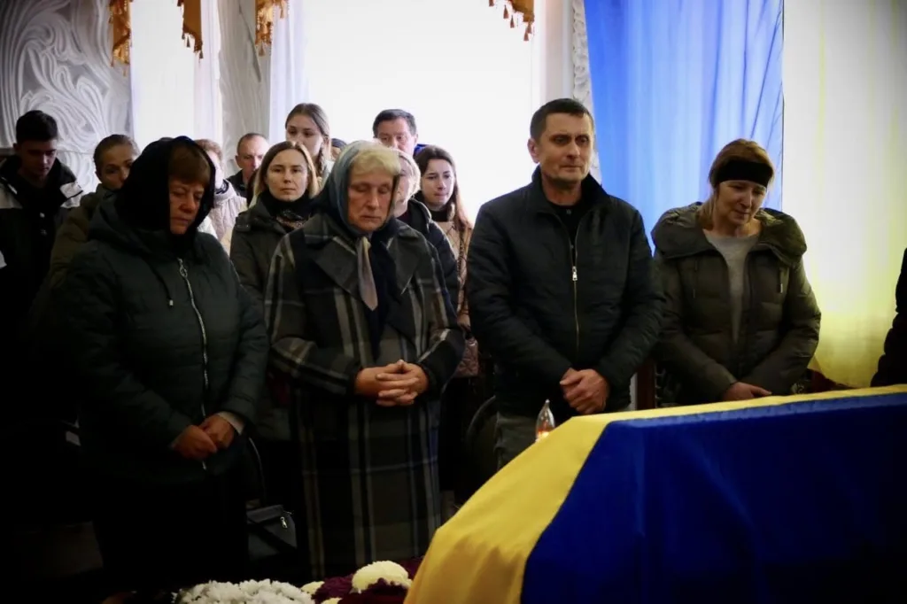 Люди прощаються біля труни, накритої прапором України