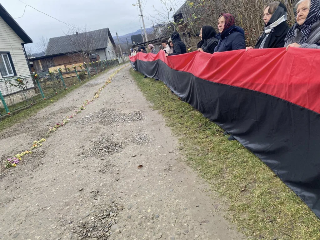 Люди тримають червоно-чорний прапор уздовж дороги