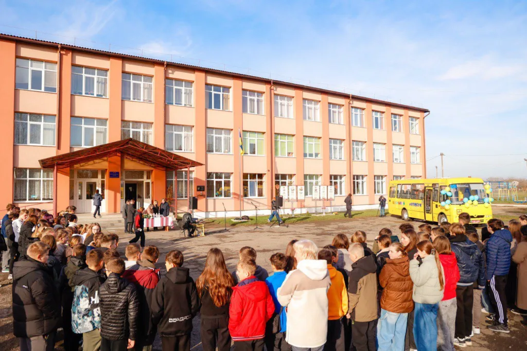 Учні перед школою та жовтим шкільним автобусом