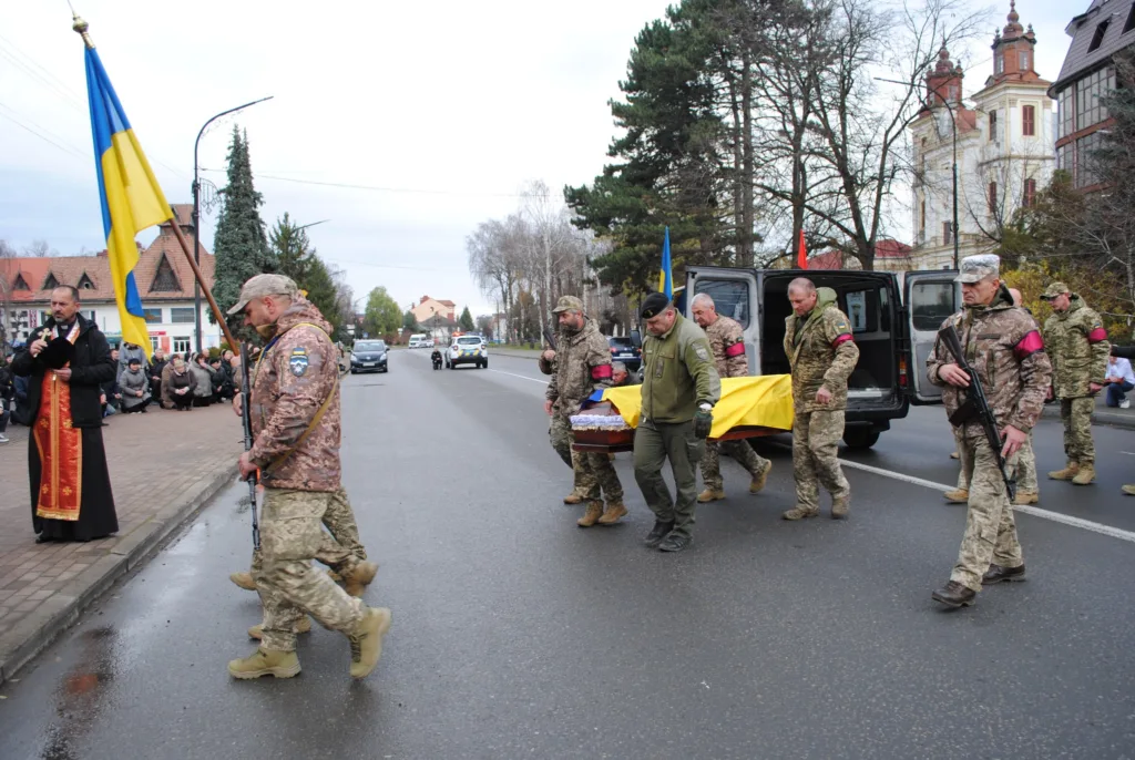 Військові несуть труну, накриту українським прапором