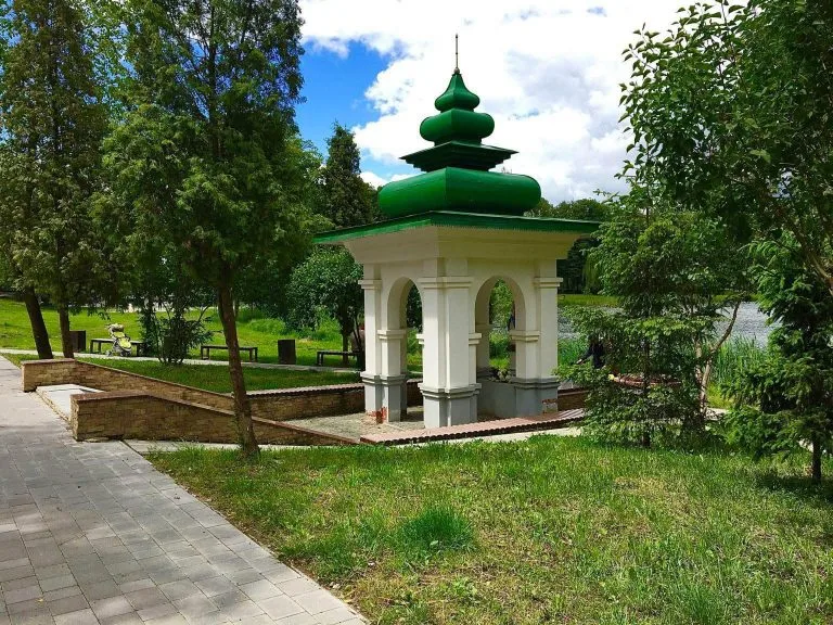 Білий павільйон із зеленою покрівлею у парку