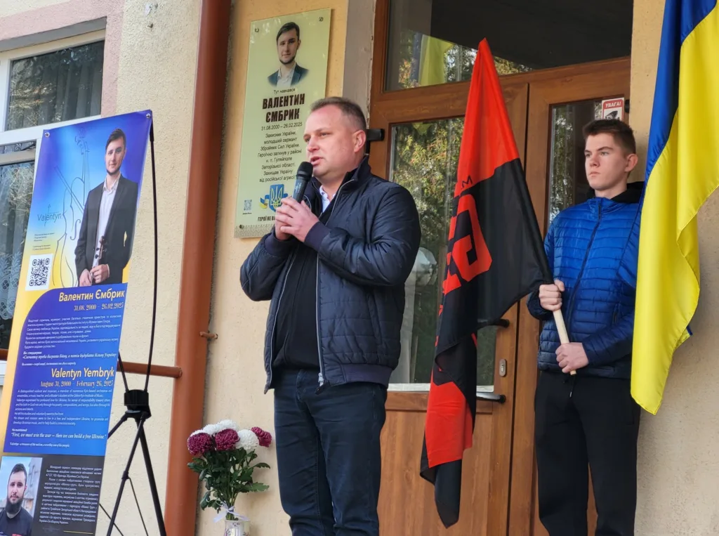 Виступ чоловіка біля меморіальної дошки героя