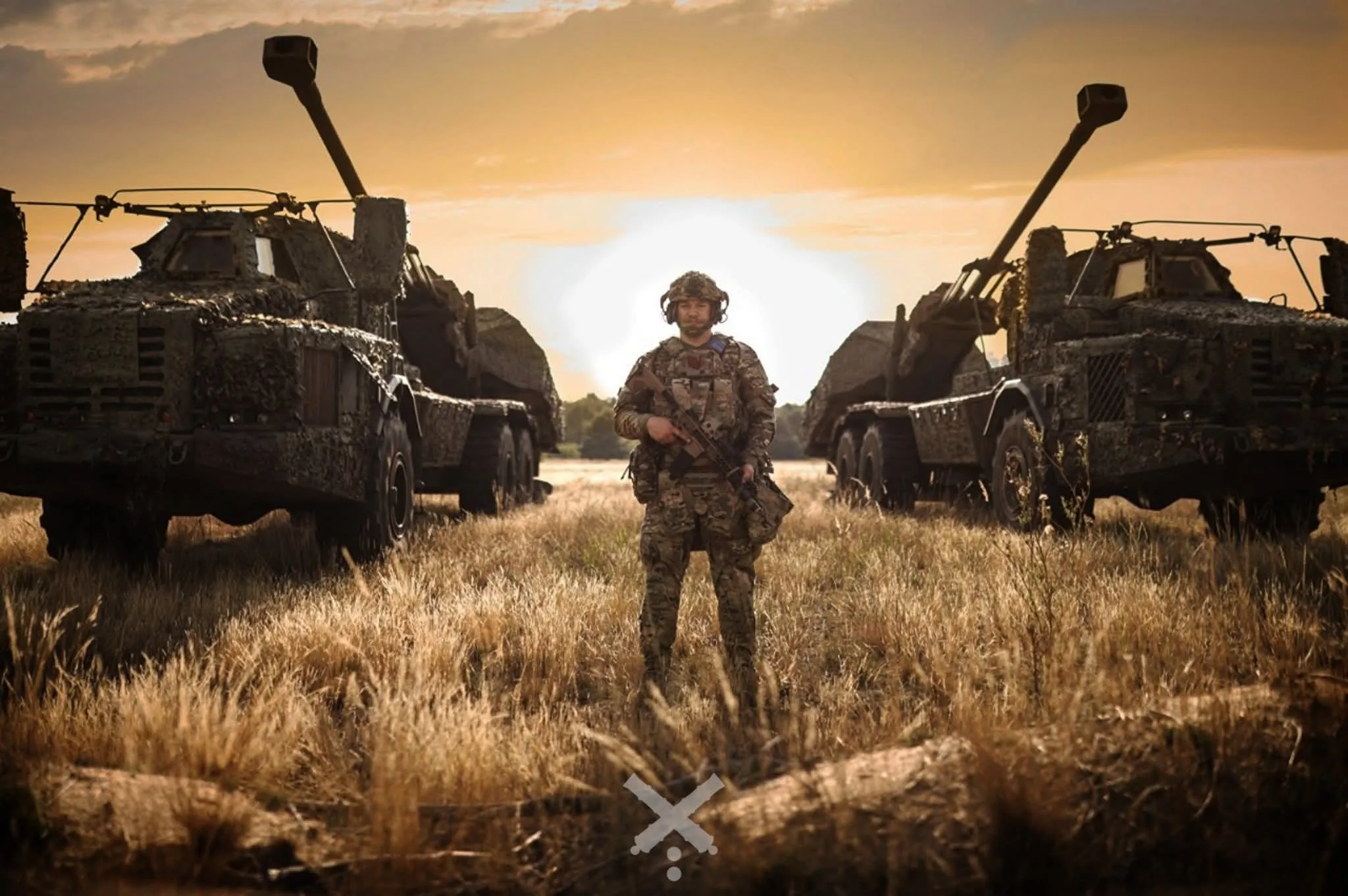 Військовий стоїть між двома самохідними гарматами на полі