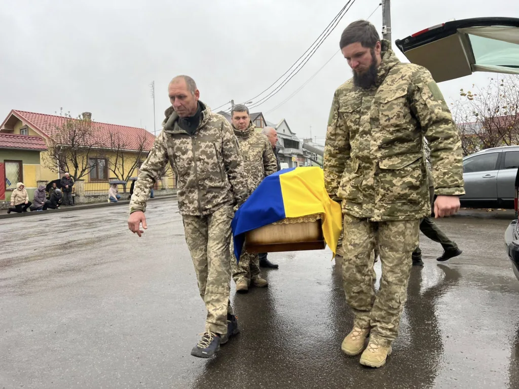 Військові несуть труну, накриту українським прапором