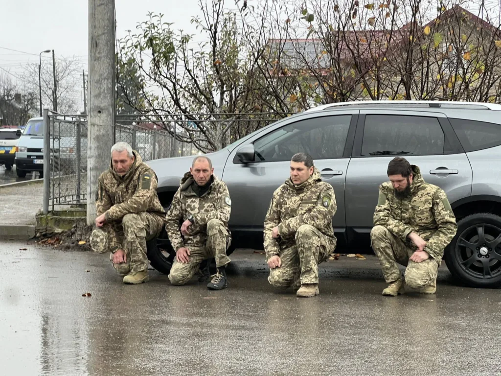 Українські військові стоять на колінах під дощем