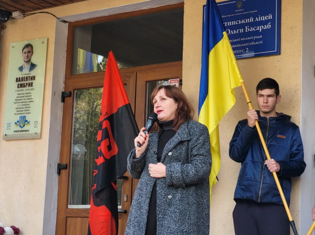 Жінка говорить біля школи з українським прапором