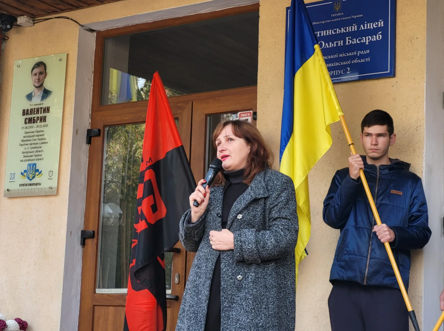 Жінка говорить біля школи з українським прапором