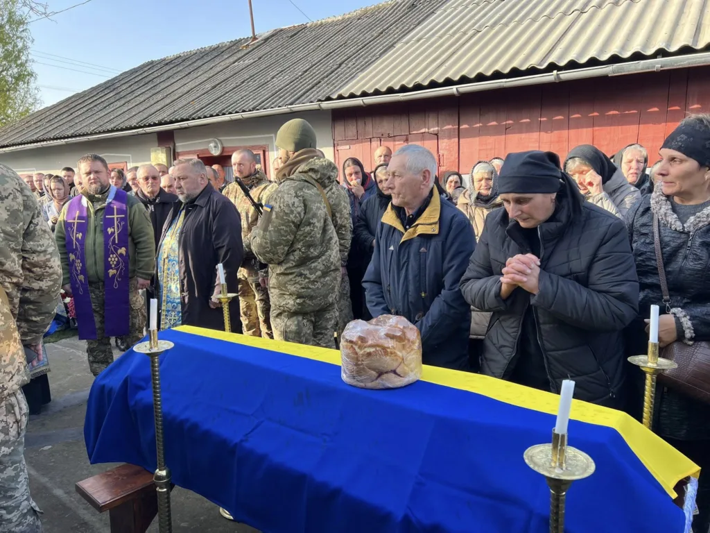 Люди прощаються з військовим, накритим українським прапором