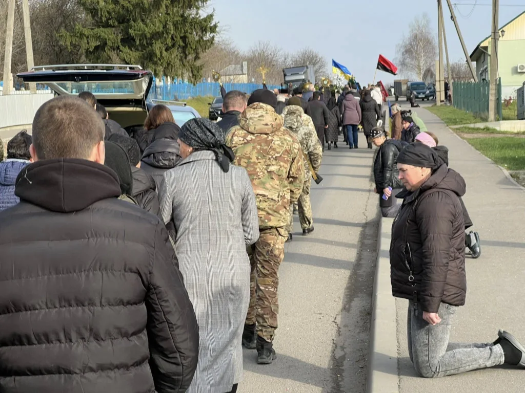 Люди на колінах під час похоронної процесії