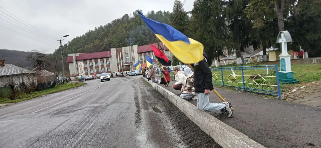 Люди з українськими прапорами стоять на колінах