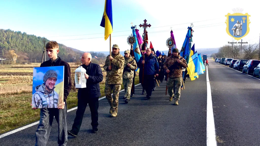 Похоронна процесія з українськими прапорами на дорозі