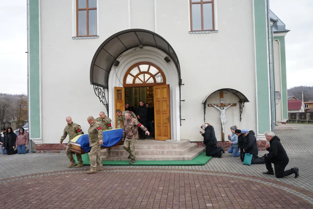 Військові несуть труну з прапором біля церкви