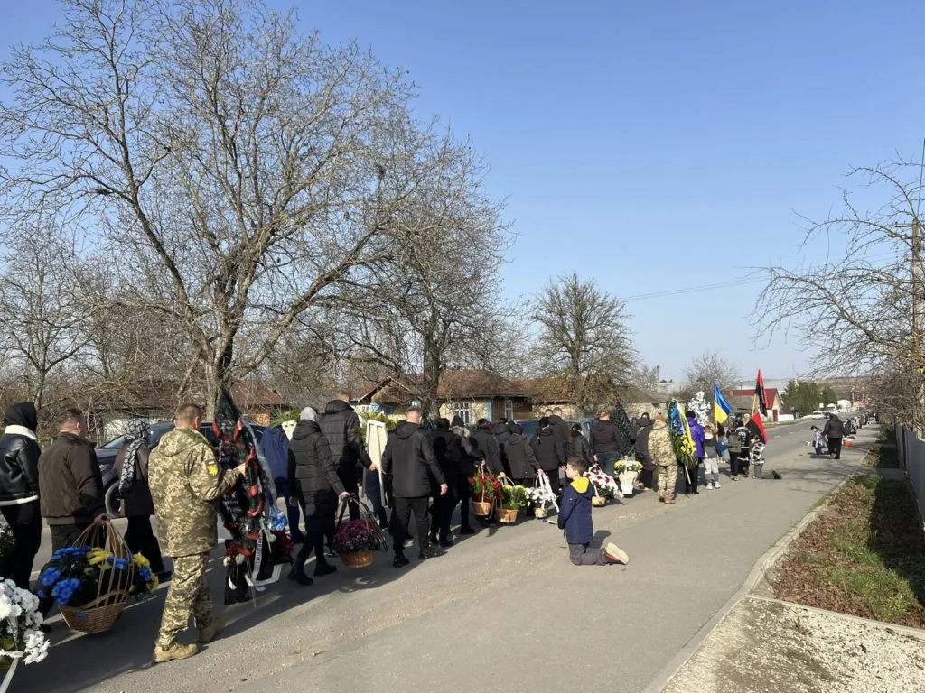 Похоронна процесія з квітами та прапорами в селі